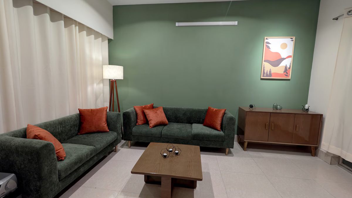 Living room with a sage-green wall, green sofa and rust cushions